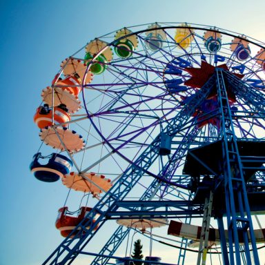 Grande roue colorée sous un ciel bleu, avec des cabines suspendues.