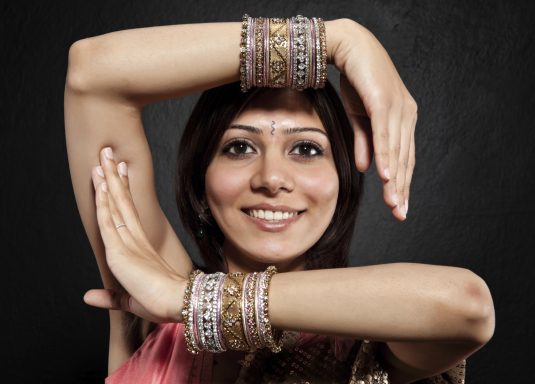 Femme souriante avec des bracelets, posant avec les bras en croix.