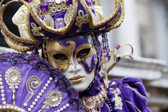 Masque de carnaval en violet et or, avec des embellissements et un grand chapeau décoré.