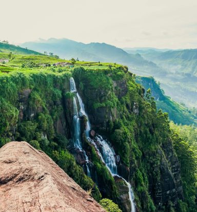 Cascades d'eau surplombant une vallée verdoyante et montagnes au loin.
